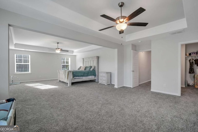 unfurnished bedroom with ceiling fan, carpet, a tray ceiling, a walk in closet, and a closet