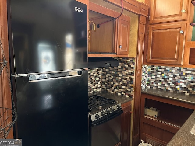 kitchen featuring ventilation hood, stainless steel gas stove, tasteful backsplash, and black refrigerator