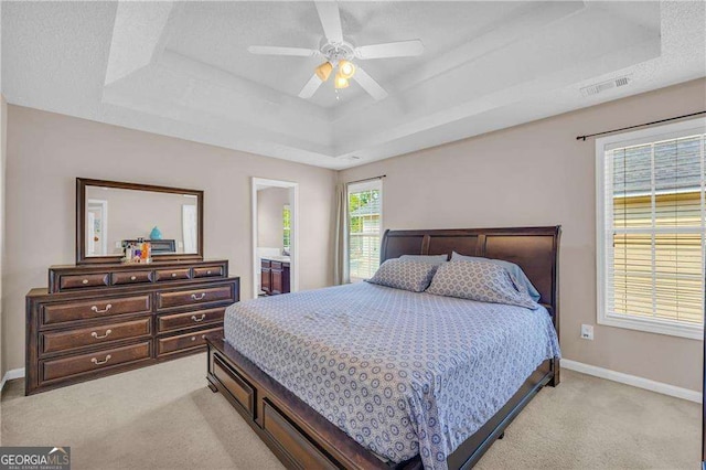 bedroom with ceiling fan, ensuite bath, a tray ceiling, and light colored carpet