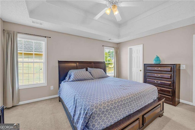 carpeted bedroom featuring ceiling fan, multiple windows, and a raised ceiling