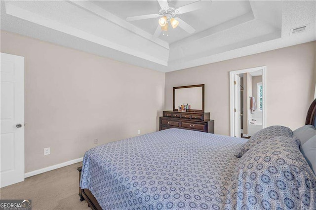 carpeted bedroom featuring ceiling fan, ensuite bathroom, and a raised ceiling