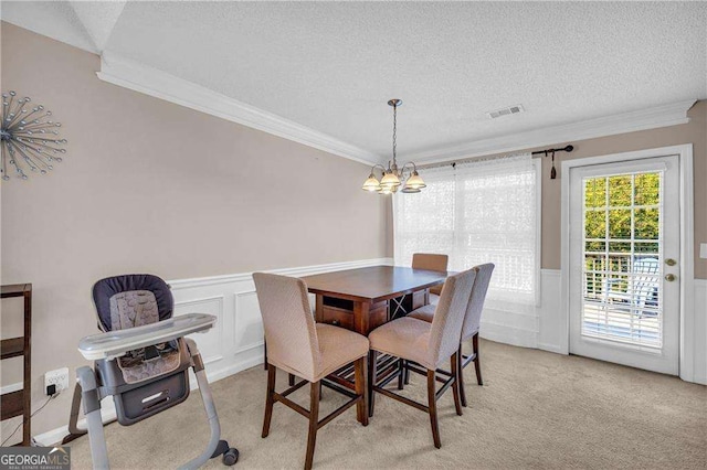 carpeted dining room with a textured ceiling, ornamental molding, and an inviting chandelier