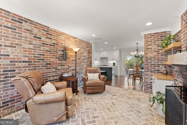 living room featuring a brick fireplace, sink, an inviting chandelier, ornamental molding, and brick wall