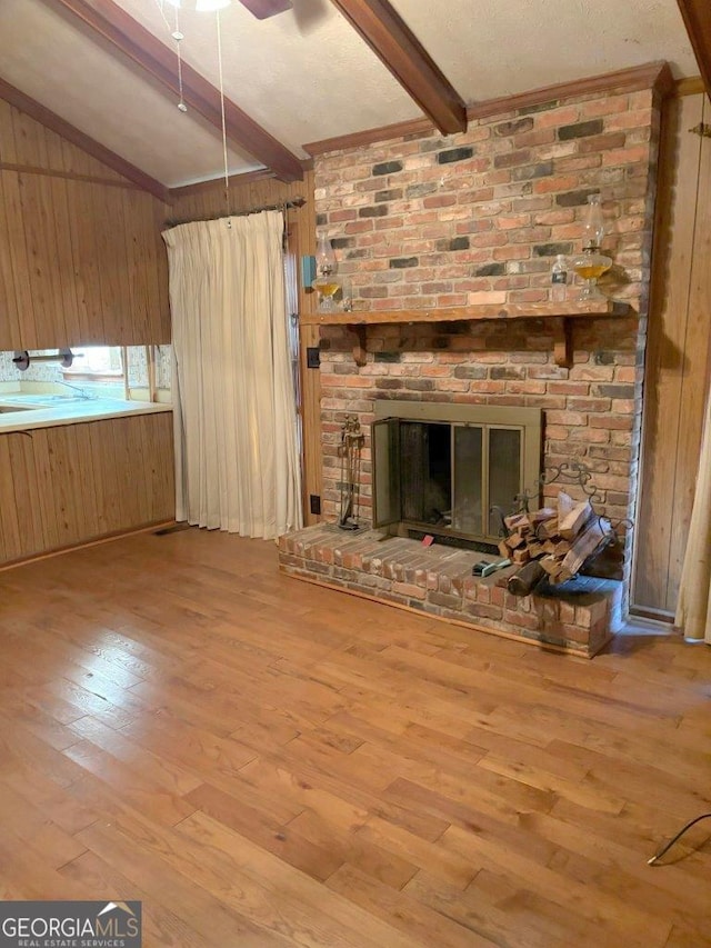 unfurnished living room featuring wooden walls, ceiling fan, light wood-type flooring, a brick fireplace, and beam ceiling