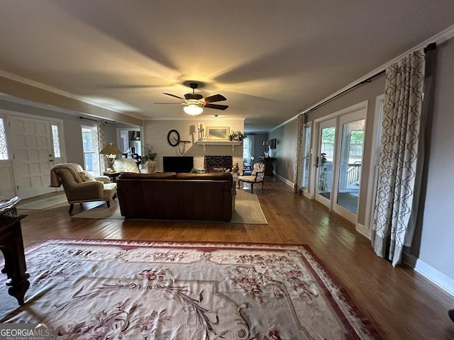 living room featuring ceiling fan, ornamental molding, wood-type flooring, and a brick fireplace