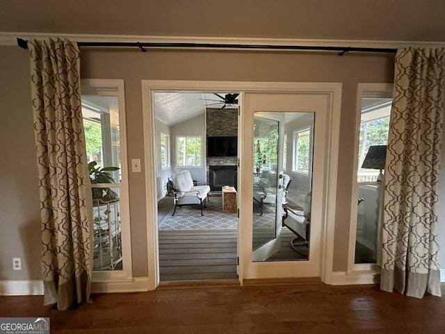 doorway to outside featuring ceiling fan, a large fireplace, vaulted ceiling, and wood-type flooring