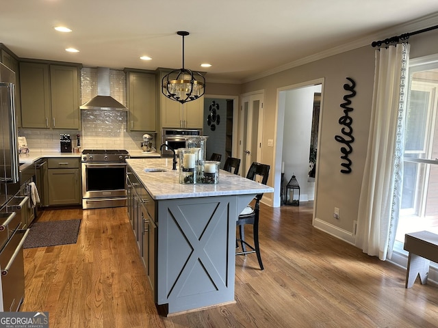 kitchen with stainless steel appliances, an island with sink, light stone countertops, wall chimney range hood, and pendant lighting