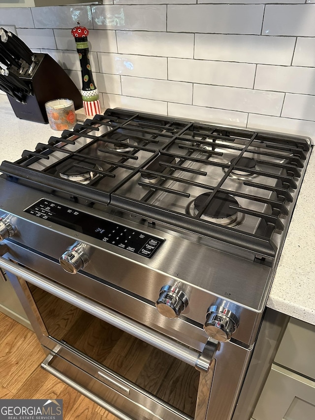 details with wood-type flooring, high end stainless steel range oven, and backsplash