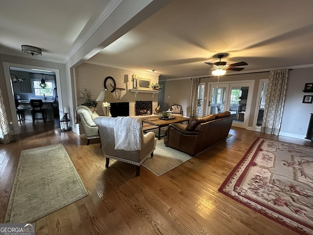 living room featuring hardwood / wood-style flooring, brick wall, ceiling fan, crown molding, and a fireplace