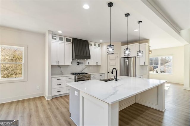 kitchen featuring white cabinetry, a center island with sink, appliances with stainless steel finishes, custom range hood, and sink