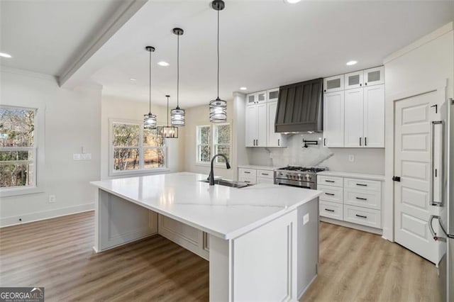 kitchen featuring white cabinets, an island with sink, sink, premium range hood, and high quality appliances