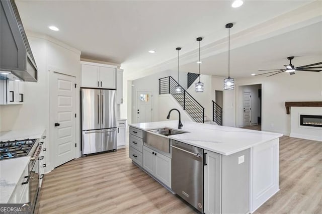 kitchen featuring ceiling fan, gray cabinets, range hood, a kitchen island with sink, and appliances with stainless steel finishes