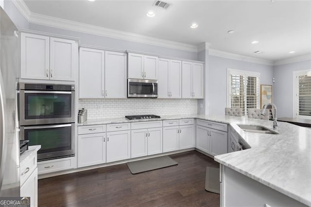 kitchen featuring visible vents, ornamental molding, light stone countertops, stainless steel appliances, and a sink