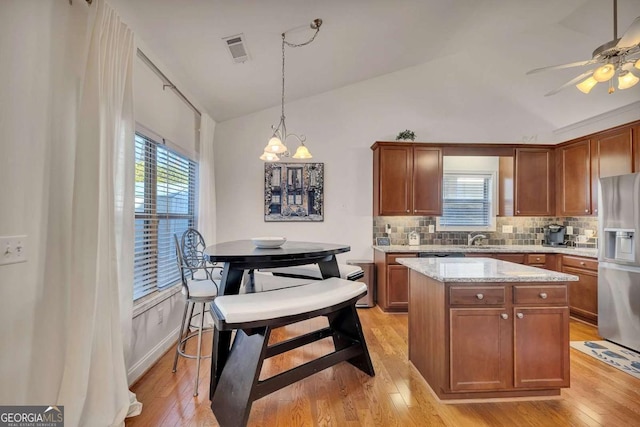 kitchen featuring lofted ceiling, decorative light fixtures, a center island, decorative backsplash, and stainless steel fridge with ice dispenser