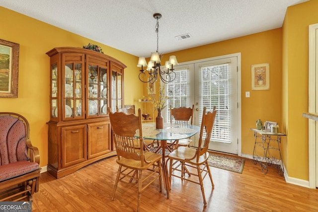 dining room featuring light hardwood / wood-style floors, a textured ceiling, and a notable chandelier