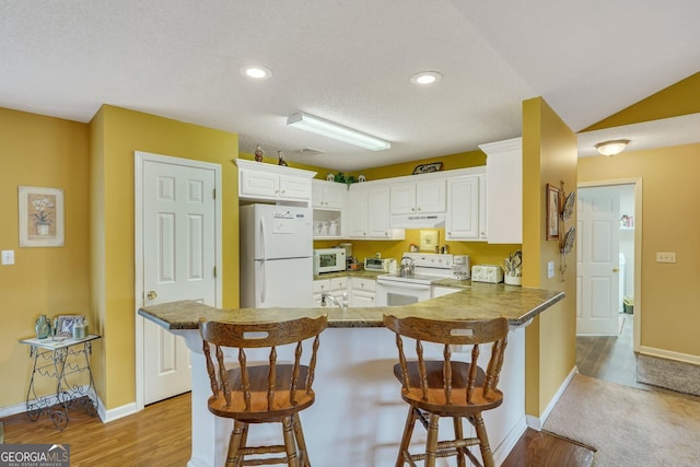 kitchen with white appliances, white cabinets, light hardwood / wood-style floors, a kitchen breakfast bar, and kitchen peninsula