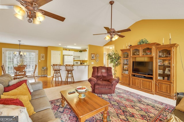 living room with ceiling fan with notable chandelier, lofted ceiling, and light wood-type flooring