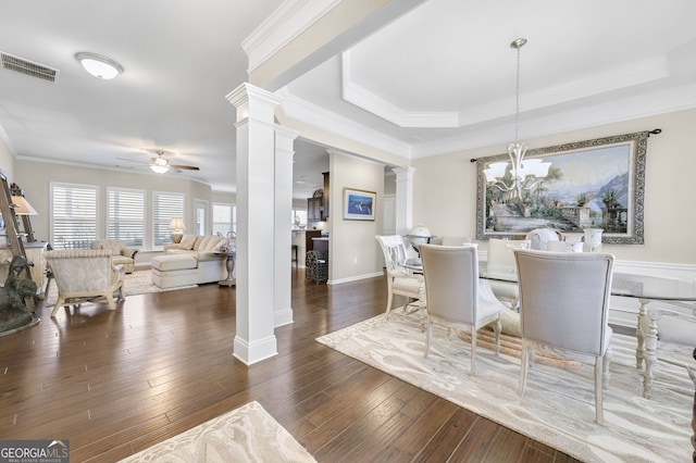 dining area featuring visible vents, a raised ceiling, hardwood / wood-style flooring, ornate columns, and ceiling fan with notable chandelier