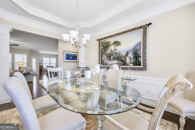 dining area with a notable chandelier, wood finished floors, wainscoting, a tray ceiling, and crown molding