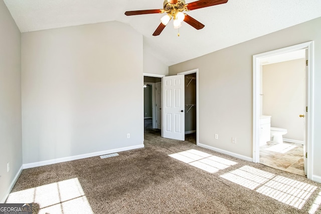 unfurnished bedroom with ceiling fan, ensuite bath, a closet, lofted ceiling, and a walk in closet