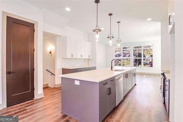 kitchen featuring white cabinets, dishwasher, sink, hanging light fixtures, and a kitchen island with sink