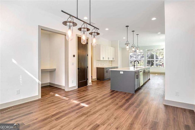 kitchen with a center island with sink, tasteful backsplash, decorative light fixtures, white cabinets, and sink