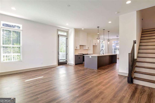 kitchen featuring decorative light fixtures, tasteful backsplash, a center island with sink, white cabinets, and dark hardwood / wood-style flooring