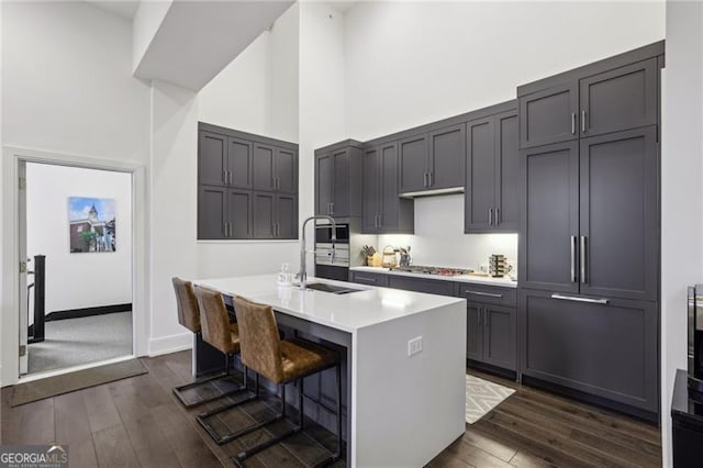 kitchen with a towering ceiling, an island with sink, sink, stainless steel gas cooktop, and a breakfast bar area