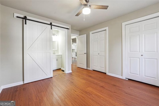 unfurnished bedroom featuring ceiling fan, a barn door, hardwood / wood-style flooring, multiple closets, and connected bathroom