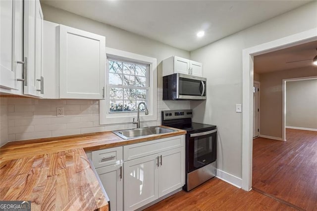 kitchen with appliances with stainless steel finishes, white cabinetry, light hardwood / wood-style floors, sink, and butcher block countertops