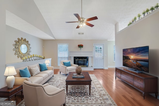 living room featuring lofted ceiling, light hardwood / wood-style flooring, a high end fireplace, and ceiling fan