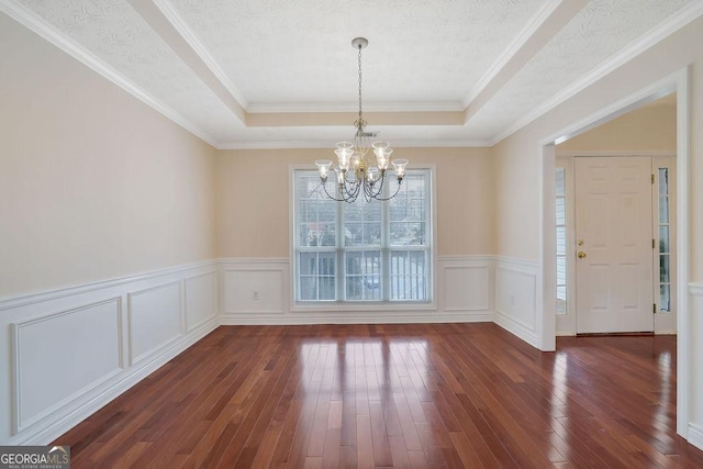 unfurnished dining area featuring a tray ceiling, dark hardwood / wood-style floors, ornamental molding, and an inviting chandelier