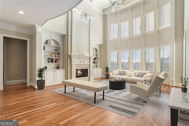 living room featuring crown molding, built in features, a towering ceiling, a fireplace, and light hardwood / wood-style floors