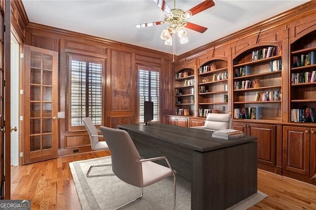 office with ceiling fan, wood walls, light wood-type flooring, and french doors