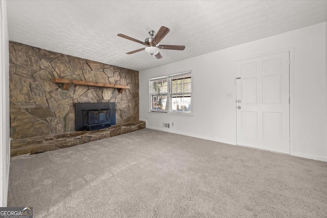 unfurnished living room featuring a textured ceiling, ceiling fan, carpet flooring, and a wood stove