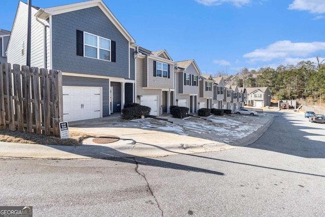 townhome / multi-family property featuring fence, a residential view, a garage, and concrete driveway
