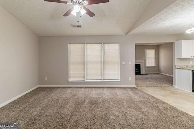 unfurnished living room with ceiling fan, light colored carpet, a textured ceiling, and lofted ceiling