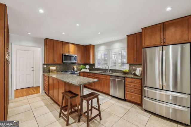 kitchen with a kitchen bar, sink, light tile patterned flooring, appliances with stainless steel finishes, and dark stone counters