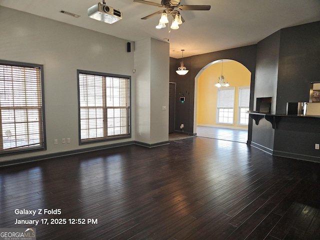 unfurnished living room with dark hardwood / wood-style floors, a wealth of natural light, and ceiling fan with notable chandelier