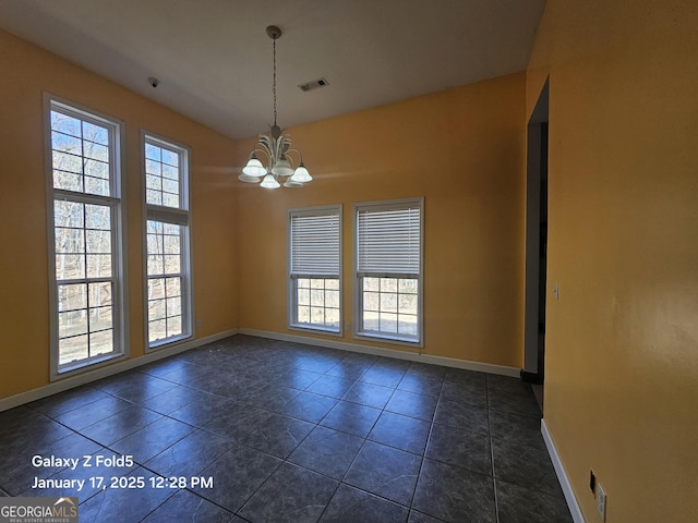 spare room featuring a healthy amount of sunlight, dark tile patterned flooring, and an inviting chandelier