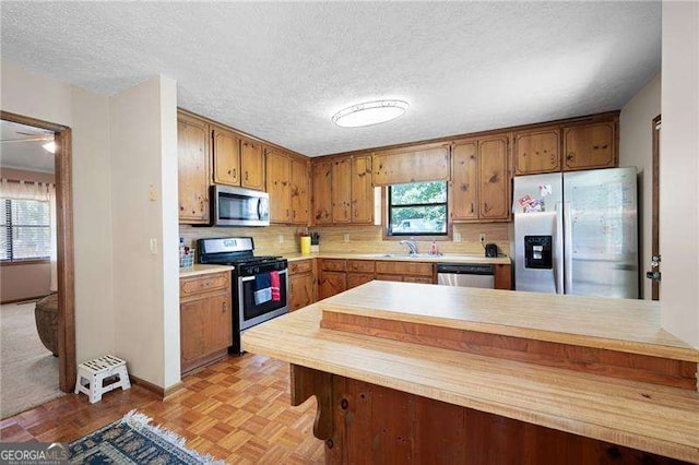 kitchen with sink, a textured ceiling, appliances with stainless steel finishes, and light parquet flooring