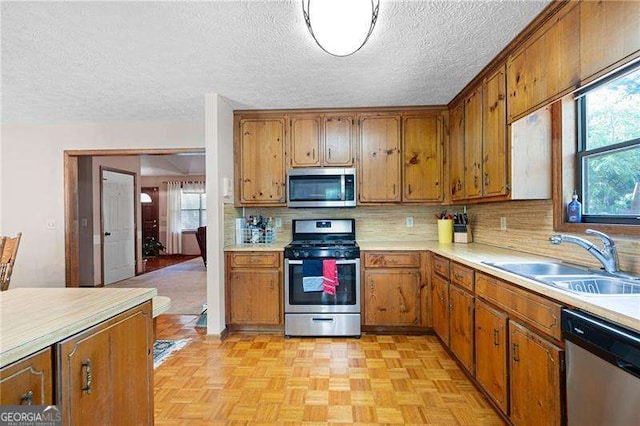 kitchen with a textured ceiling, light parquet flooring, stainless steel appliances, tasteful backsplash, and sink