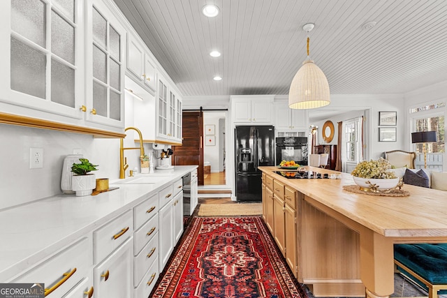 kitchen featuring white cabinets, black appliances, wood counters, hanging light fixtures, and a barn door