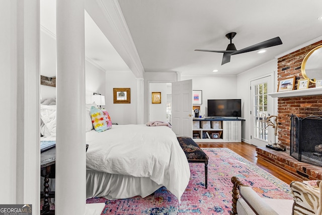 bedroom featuring ceiling fan, a brick fireplace, wood-type flooring, and crown molding