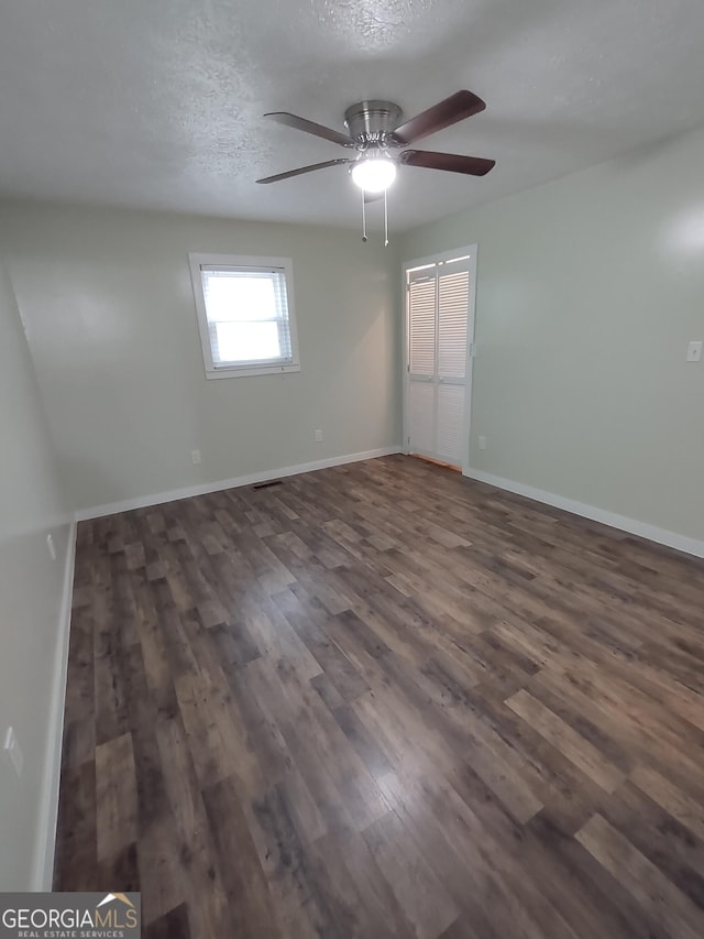 empty room with ceiling fan, dark wood-type flooring, and a textured ceiling