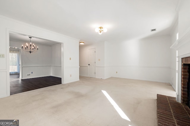 unfurnished living room featuring a fireplace, a chandelier, carpet flooring, and crown molding