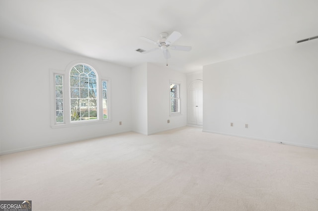 empty room featuring ceiling fan, light colored carpet, and a wealth of natural light