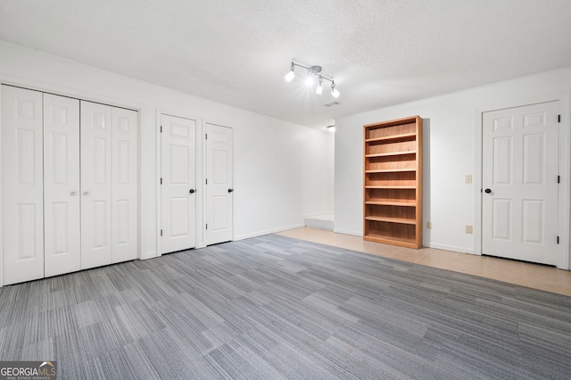 unfurnished bedroom with a textured ceiling and multiple closets