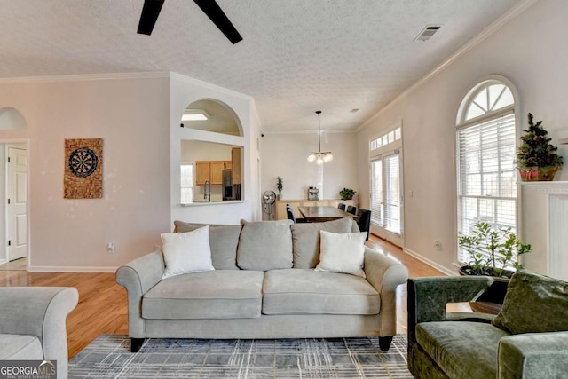 living room with a textured ceiling, crown molding, ceiling fan with notable chandelier, and wood-type flooring