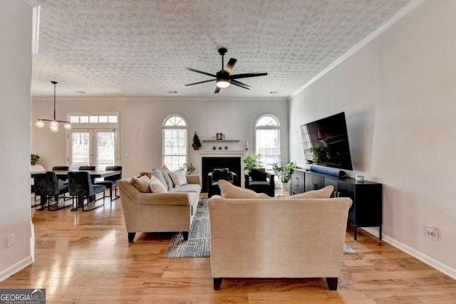 living room with a healthy amount of sunlight, ceiling fan with notable chandelier, crown molding, and light hardwood / wood-style floors